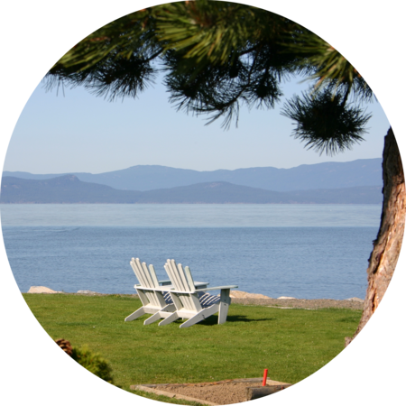 Circular image of Parksville beachside with two white lawn chairs on top of grass with tree in background
